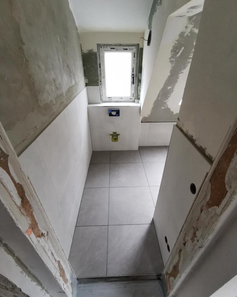 Unfertiges, gefliestes Badezimmer mit Vorwandinstallation und Fenster